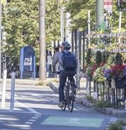 A cyclist rides in a flex-post separated bike lane in Porter Square, next to an outdoor dining patio filled with hanging flower baskets