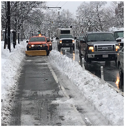 An orange DPW truck with a plow attachment removes snow from a separated bike lane