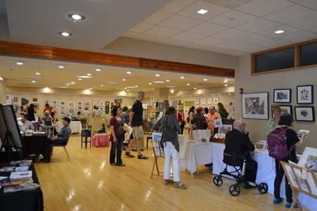 A large venue showcases many tables of artwork during Cambridge Open Studios.