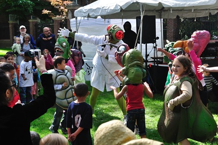 A performer dressed as an human-sized fly scientist dances with a crowd of youngsters dressed in oversized insect and monster costumes.