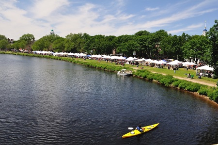 A long overall photo from across the river of a busy Cambridge River Festival. A lone kayaker watches from the water.