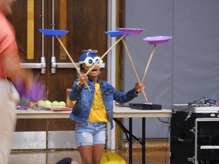 A young volunteer wears a silly mask while performing a plat spinning trick