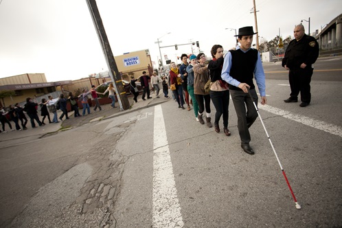 Carmen Papalia: Blind Field Shuttle - A line of people crossing the street with security guard