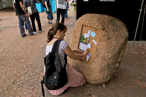 Paul Ramirez Jonas, Publicar - A woman pinning a not to a bulletin board embedded in stone
