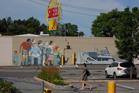 A far shot of the Beat the Belt mural featuring the Shell sign and a passerby walking