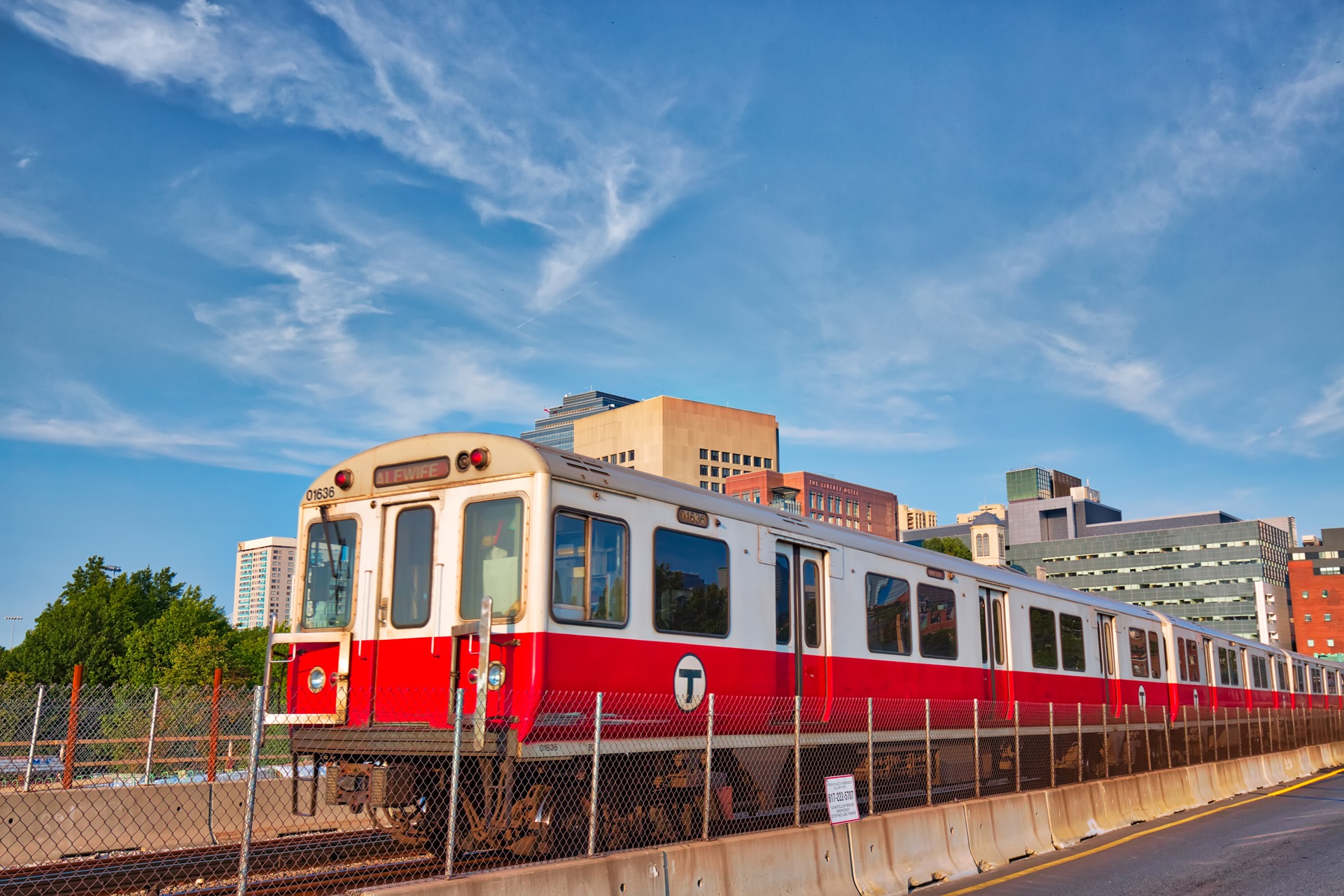 An MBTA red line train runs down surface tracks under a bright blue sky