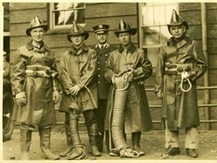 old time firefighters in gear holding equipment