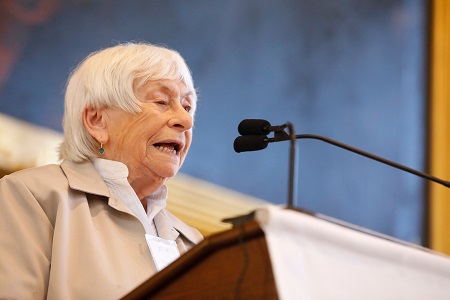 A headshot of Holocaust Survivor Esther Adler speaking from being a podium