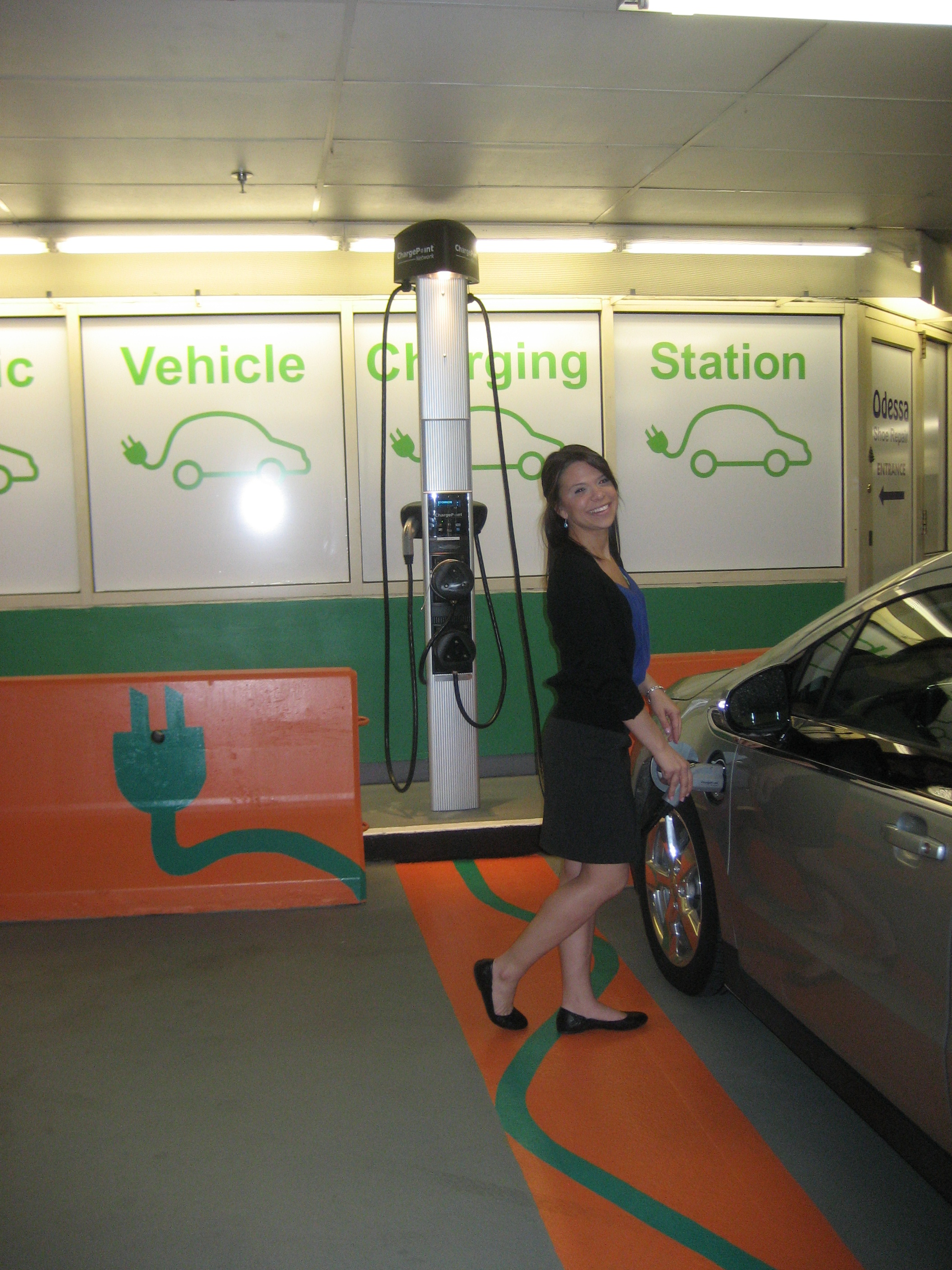 A woman charging an electric vehicle at the state-funded EV charging station in the Cambridgeside Galleria garage