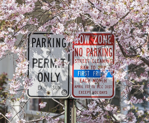A "Parking by Permit Only" sign and "Tow Zone: No Parking Sign", side by side