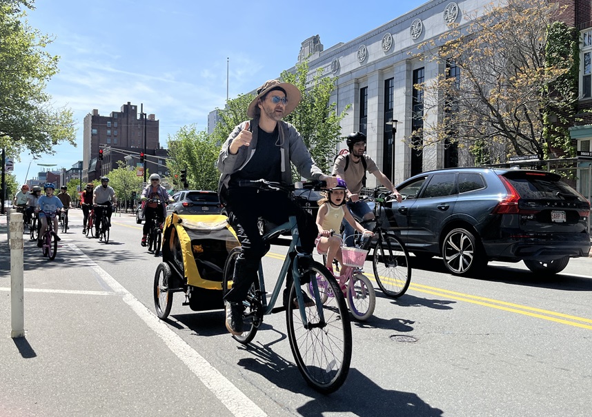 A person rides a bike with a trailer attached and a child inside.