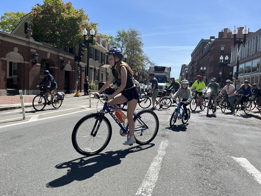 A teen rides their bike through Harvard Square. Others from the bike ride are close behind.