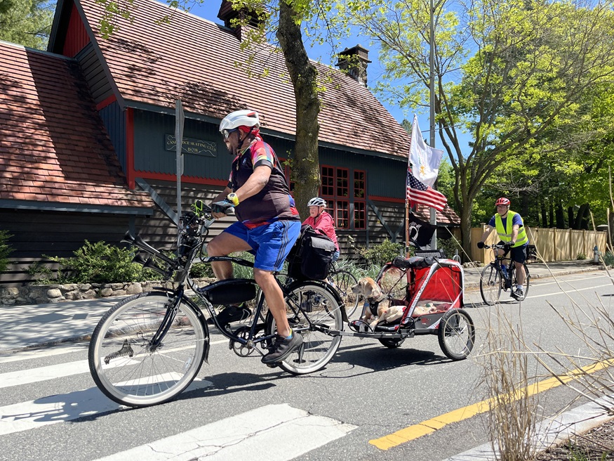 A biker with a dog trailer and flags rides past the Cambridge Skating Club building.