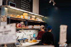 This is a picture of employees at the counter of Formaggio Kitchen. Employees are cutting cheese for customers.