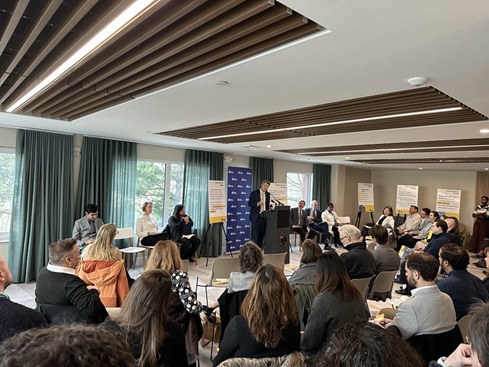 Yi-An Huang stands at a podium in front of a blue City of Cambridge backdrop and addresses a seated audience at 52 New Street to announce the release of the Affordable Housing Trust 5 Year Report