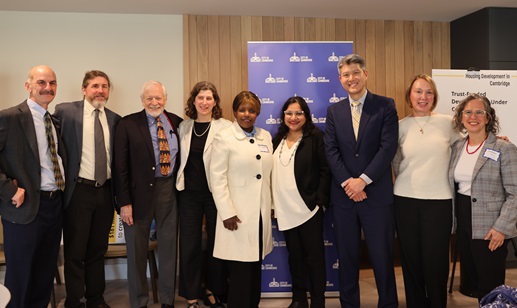A group of people in business attire standing and smiling in front of a City of Cambridge backdrop