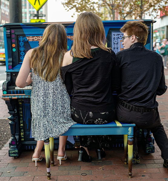 Three people playing a public piano