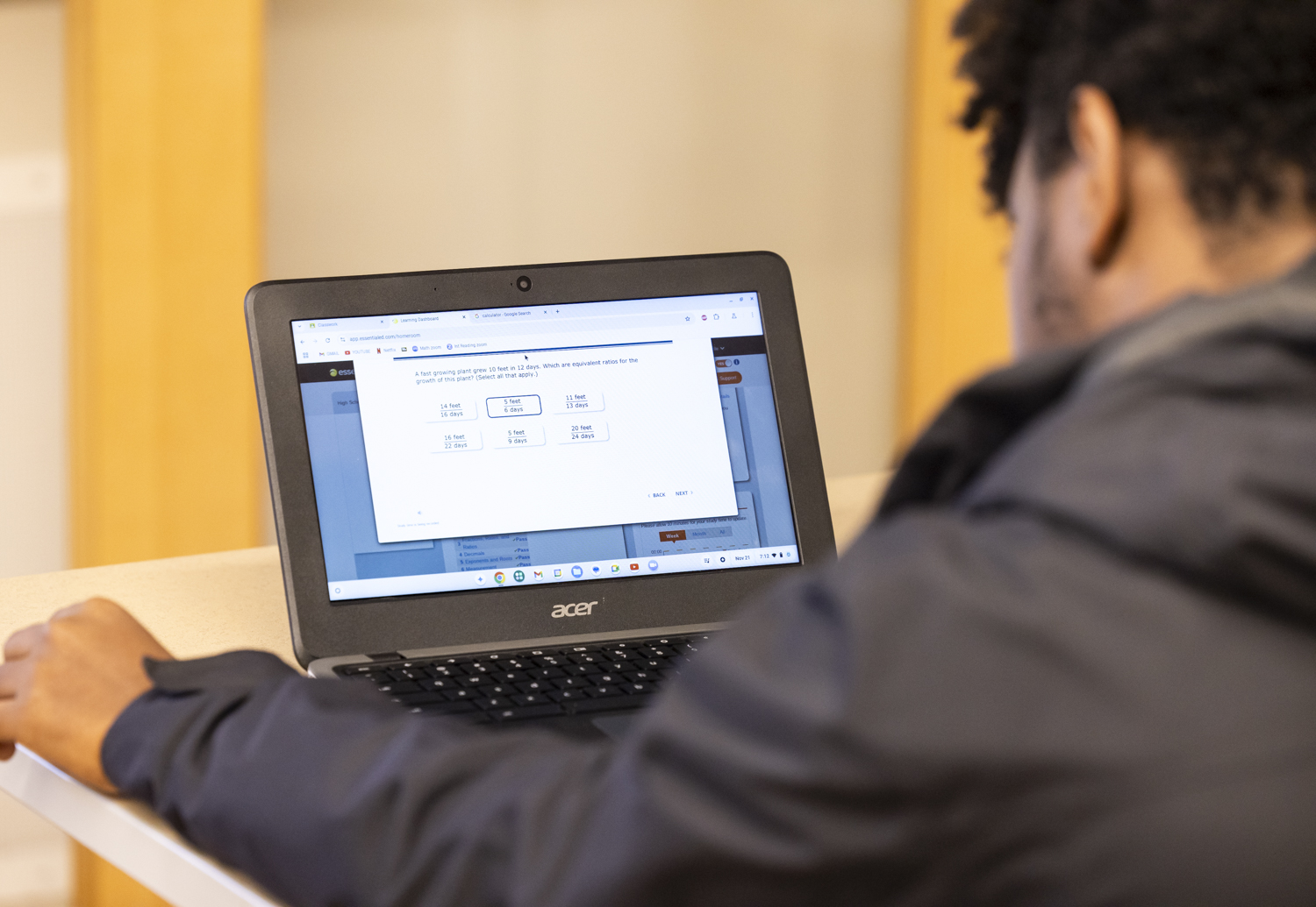 A student seated at a desk is looking at a laptop screen