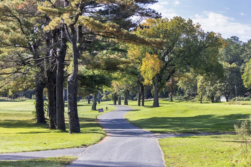 A paved path winding through trees and the golf greens.