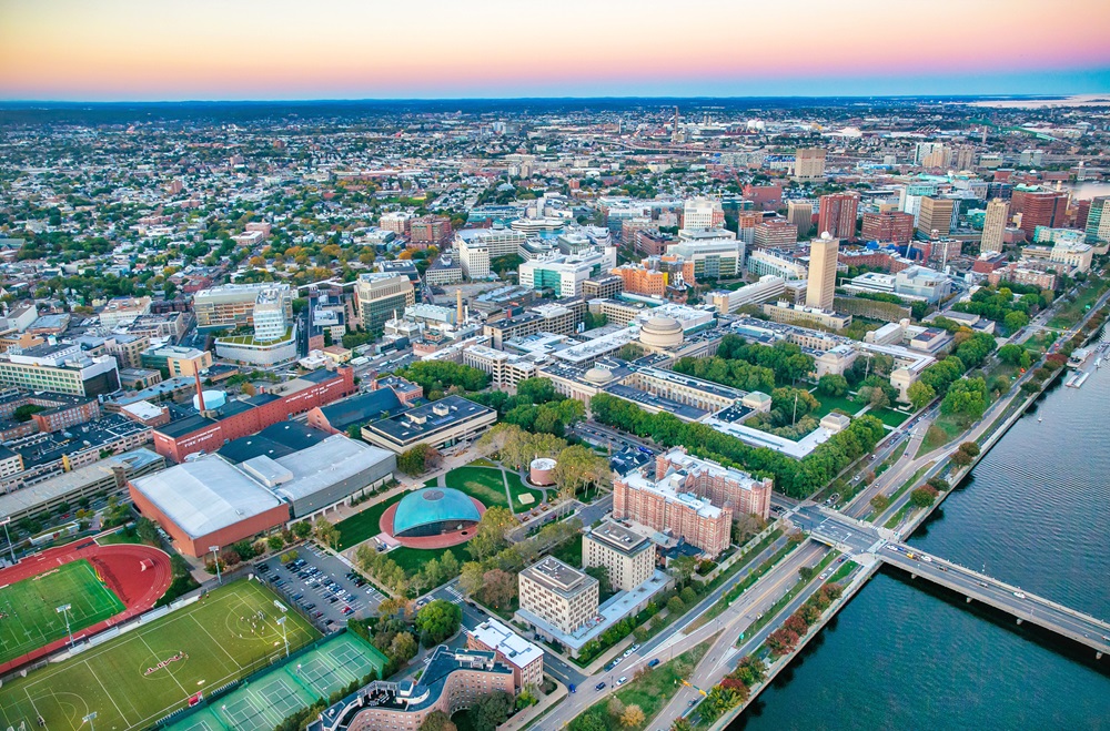 MIT campus with athletic fields, academic buildings, and a riverfront roadway.