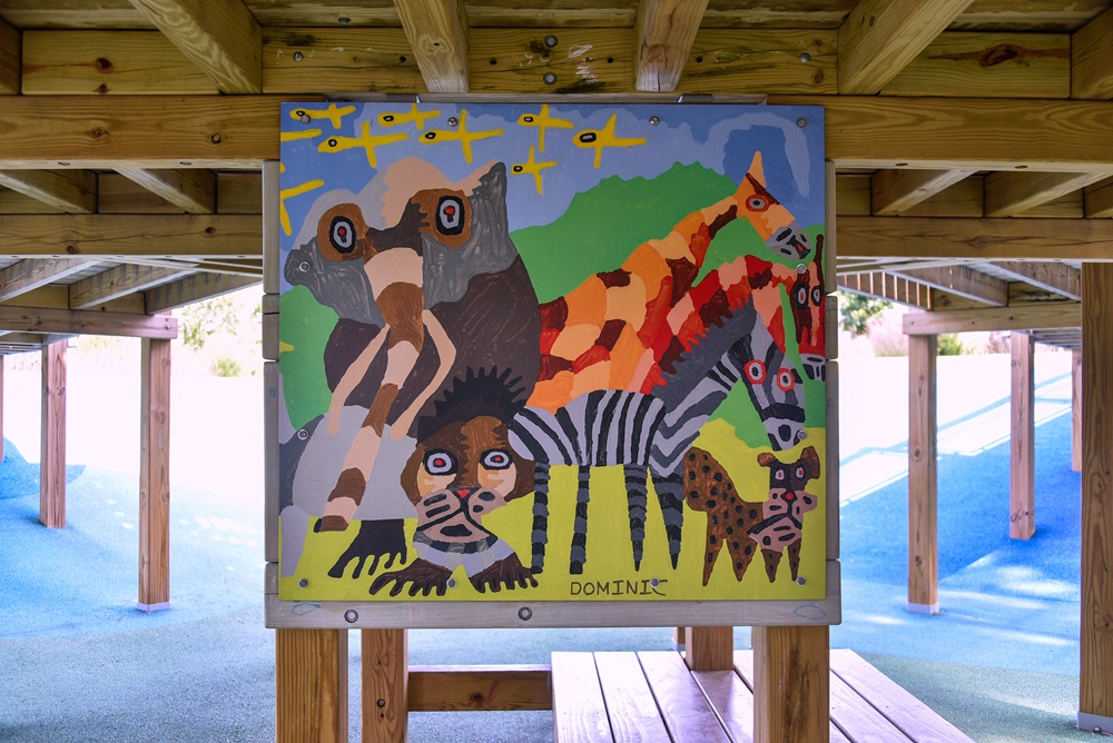 A colorful abstract painting of different animals hangs onto a structure of the Universal Design Playground.
