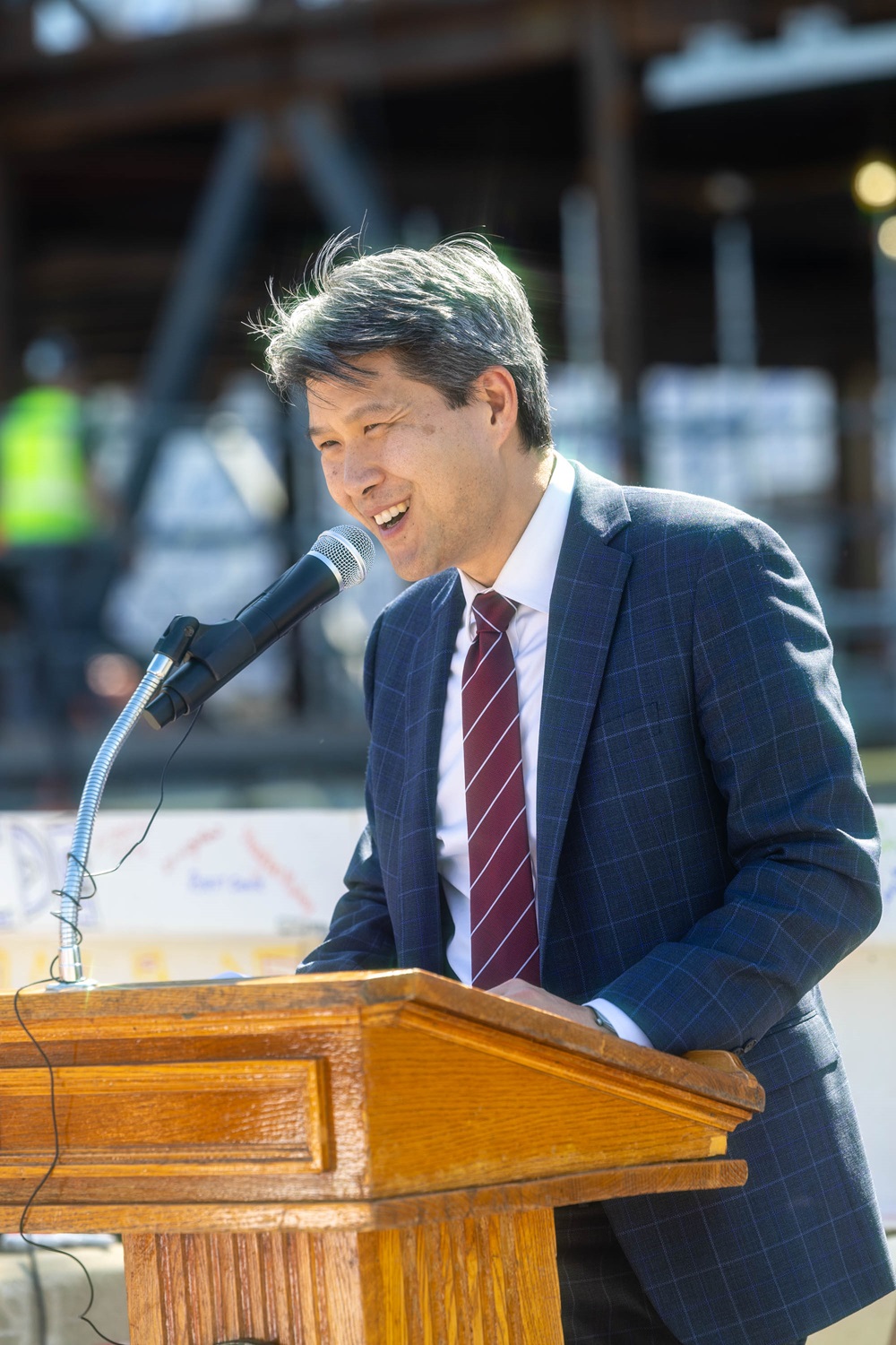 Cambridge City Manager Yi-An Huang speaking at a podium during an outdoor event.