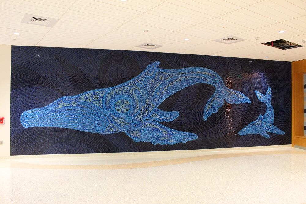 A large mosaic mural depicting two humpback whales, adorned with intricate patterns, displayed on a wall.