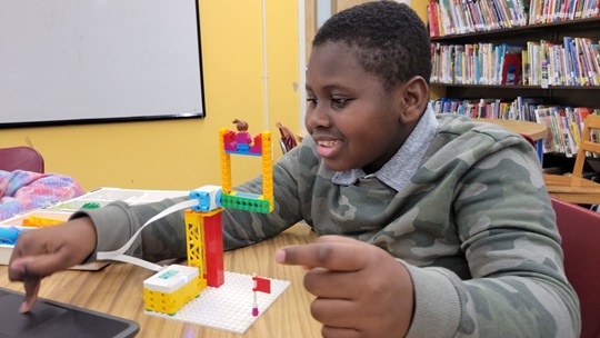 A young boy follows instructions on his laptop while building legos