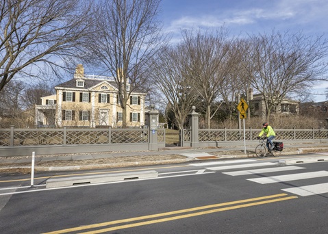 A cyclist rides their bike in the two-way separated bike lane on Brattle Street in front of the historic Longfellow House.