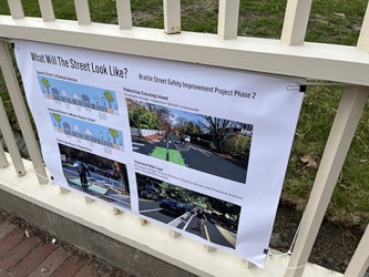 Photo of a poster on a fence. The title is "What will the street look like?" and the poster includes mock-ups of the two-way bike lane, a photo from Phase 1, and street-level views of the layout of the street, with parking, vehicle travel lanes, and separated bike lanes.
