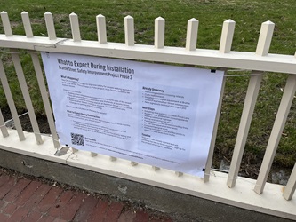 Photo of a poster hung on a fence titled "What to Expect During Installation." Headlines include "What's Happening?", "What to Expect During Construction", "Already Underway", "Next Steps", and "Timeline