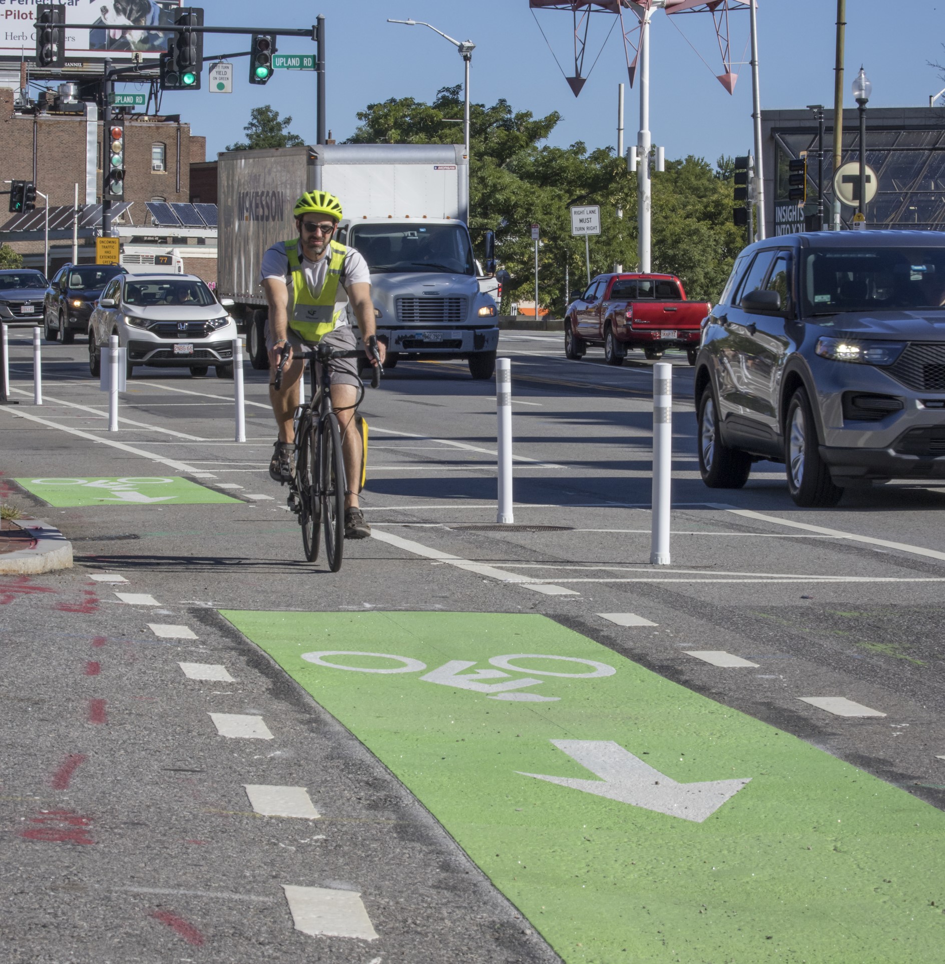 A cyclist rides in a flex-post separated bike lane in Porter Square. He is headed toward a section of the bike lane that is painted green to indicate to cars that bikes have the right of way.