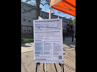 Photo of a poster board in front of a tent. The board includes information about the Main Street Safety Improvement Project limits, changes, schedule, and website.