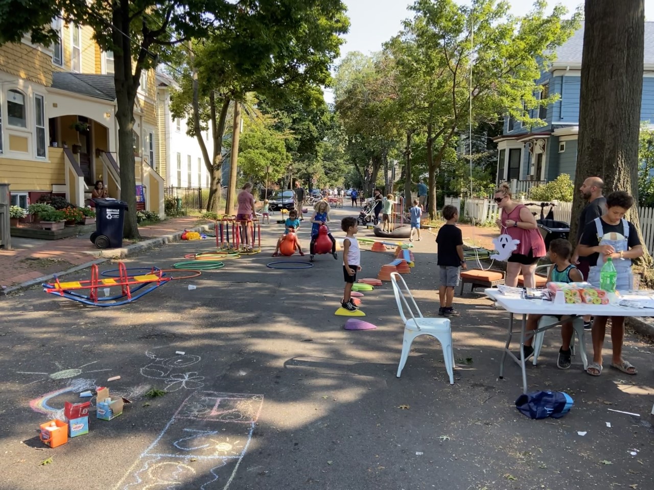 Block Party on a Cambridge street shows a scene of children of various ages playing with Play Street items