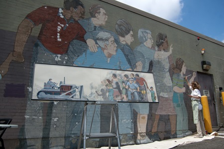 A framed illustration of the mural concept in front of the mural mid-restoration