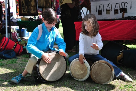 Two girls try out a few drums at a featured booth during Cambridge River Festival.