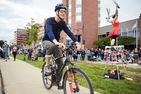 A young man rides by a performing artist on his bike