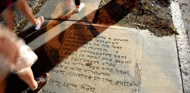 People walk next to Molly Lynn Watt's poem, which has been imprinted in a sidewalk along Prospect Street in Cambridge.