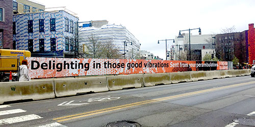 A scrim featuring text from Cambridge Arts' Sidewalk Poetry program wraps a construction site around Lafayette Square and Massachusetts Avenue in Central Square, April 2019.
