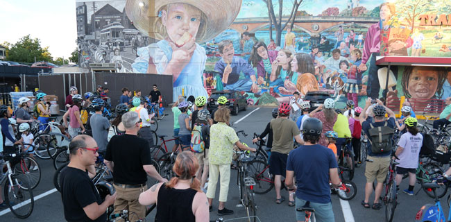David Fichter speaks about his mural “Sunday Afternoon on the Charles” on the Memorial Drive side of Trader Joe’s during a July 2022 bike tour.