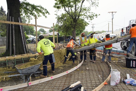 Several workers overseeing the pouring on concrete into the sidewalk mold