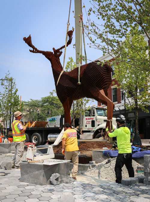 A crane lowers Mark Reigelman's “Edge of the Forest,” a 12-foot-tall steel sculpture of a deer, into Cambridge’s Inman Square, 2023.