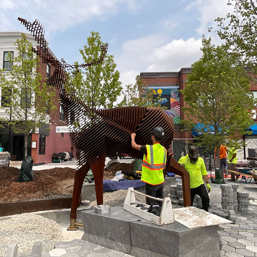 Workers install Mark Reigelman's “Edge of the Forest,” a 12-foot-tall steel sculpture of a deer, at Cambridge’s Inman Square, 2023.