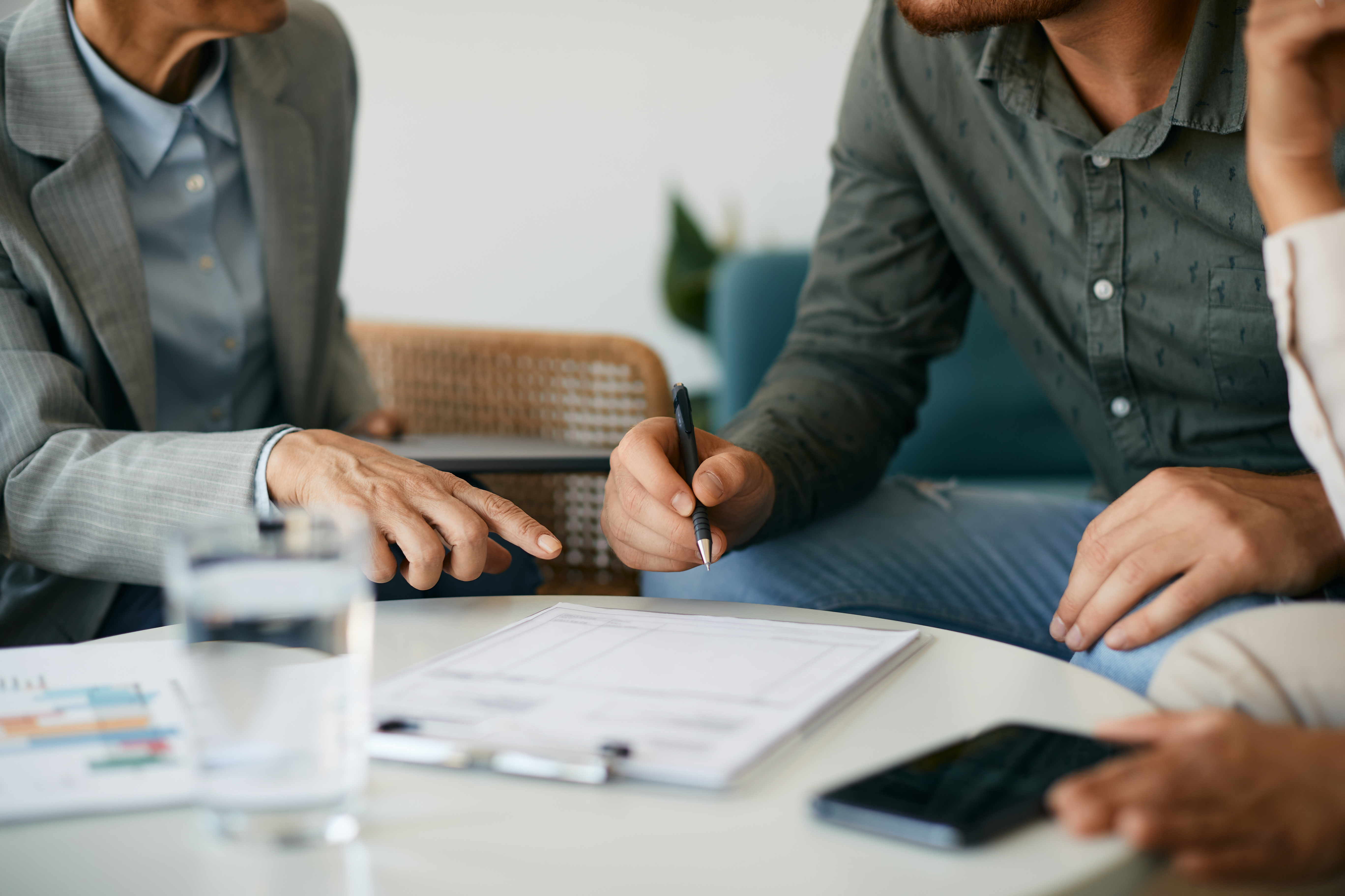 Tight shot of three people sitting around a table with a form on a clipboard, one person points to a spot on the form while another holds a pen