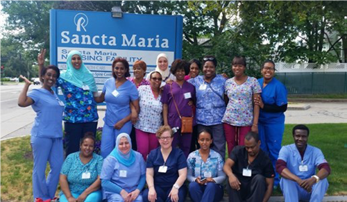 Photo of CNA Training Program graduates posing in a group photo in front of a sign that reads "Sancta Maria"