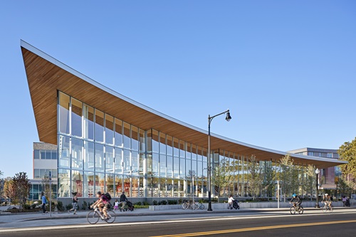 Photo by Robert Benson Photography of cyclists and pedestrians passing by the Valente Branch Library, part of the King Open/Cambridge St. Upper School and Community Complex