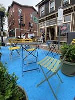 tables and chairs on blue painted pavement on an urban street surrounded by plantings