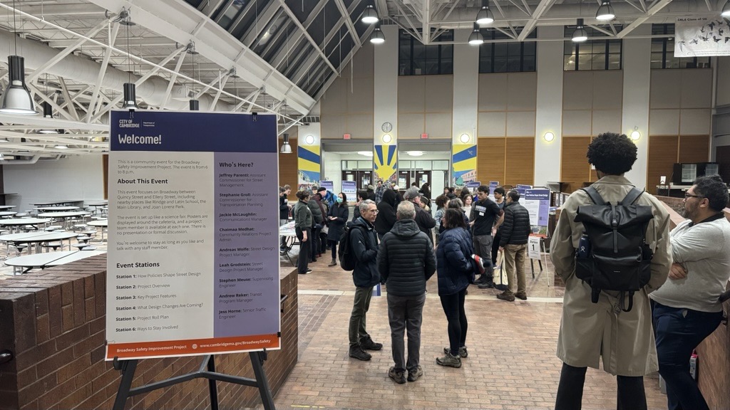 people standing around inside a school cafeteria. in the foreground a welcome board on an aisle 