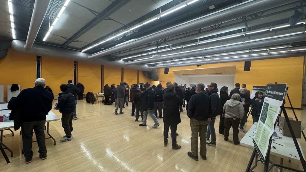 20-30 people mostly wearing black walking around a gym , boards and tables in the foreground
