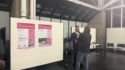 two people speaking in a gallery in front of two boards hung on a white gallery wall